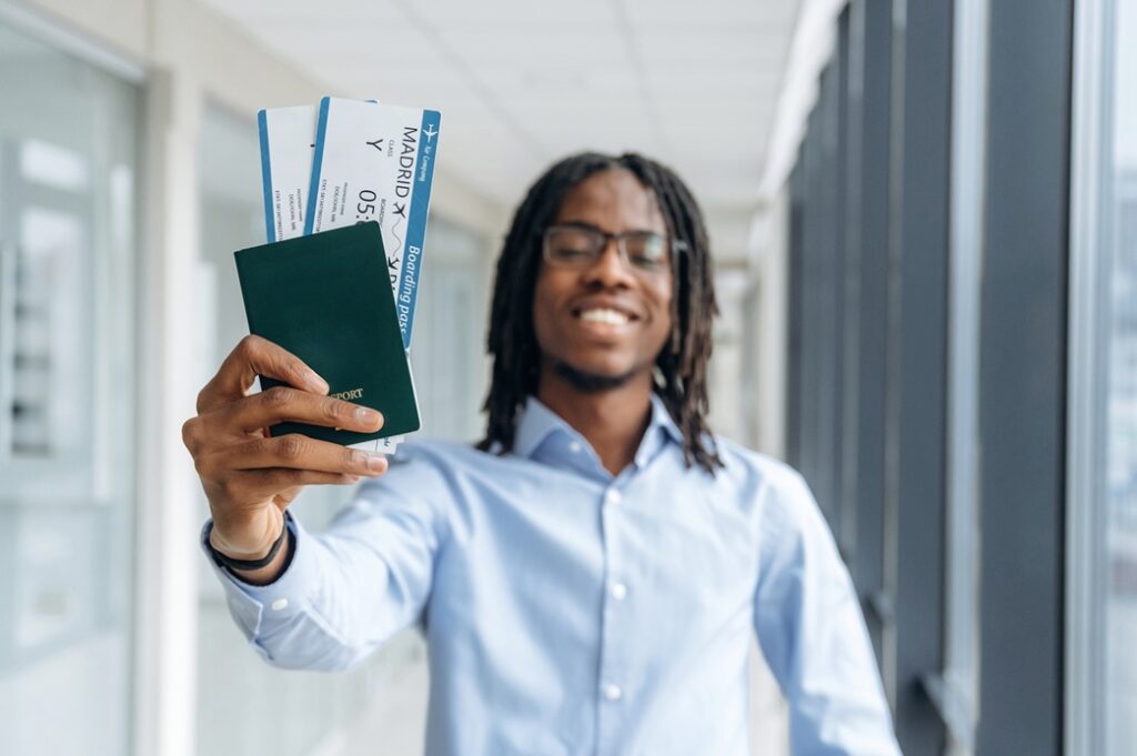 Smiling Black man holding a passport and Madrid boarding passes in a bright terminal