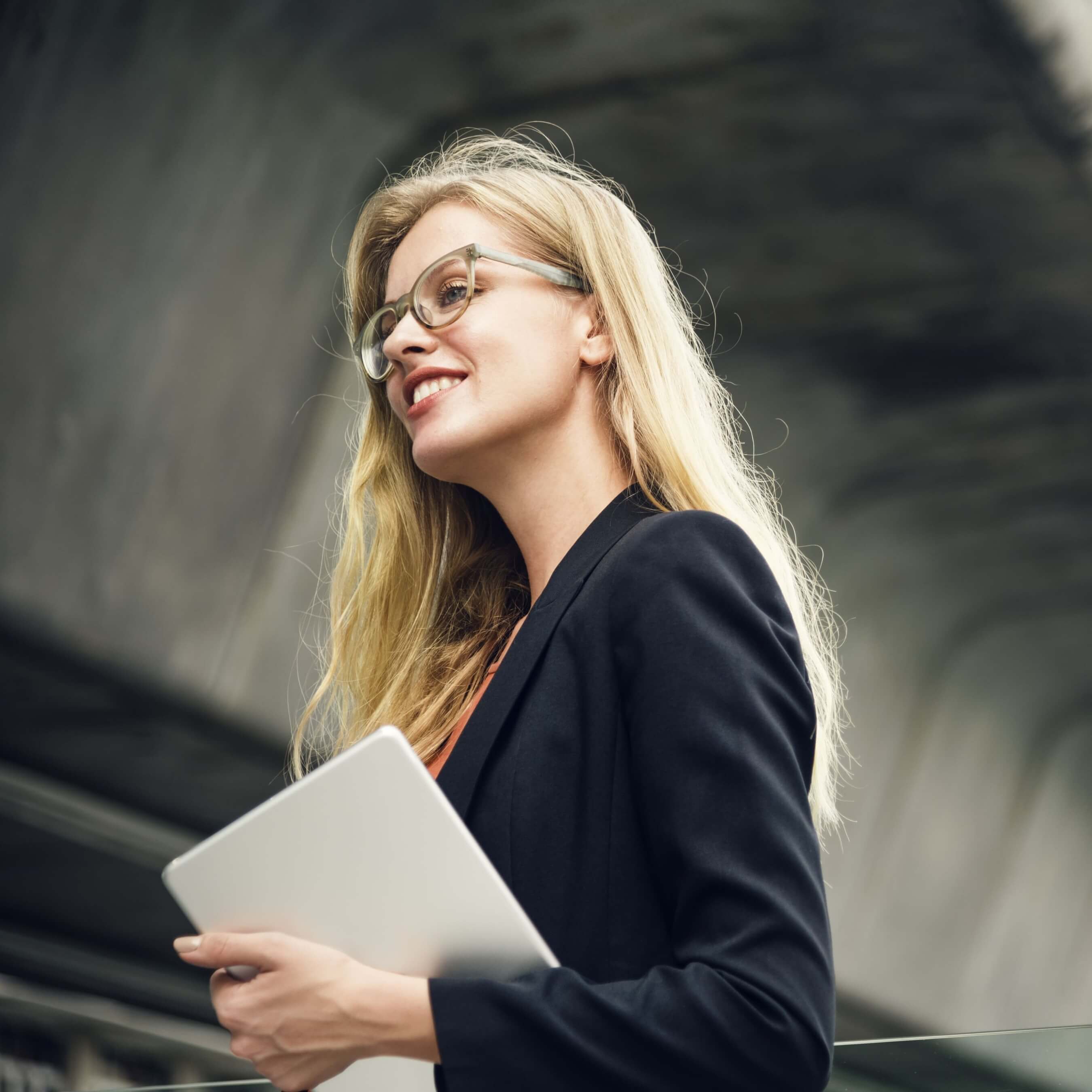 Professional woman with glasses holding a tablet in a modern outdoor setting