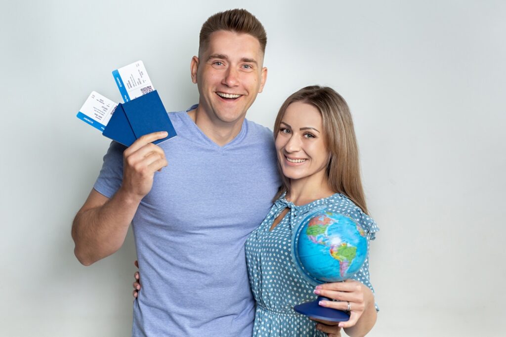 Smiling couple holding blue passports, boarding passes, and a small globe against a white background